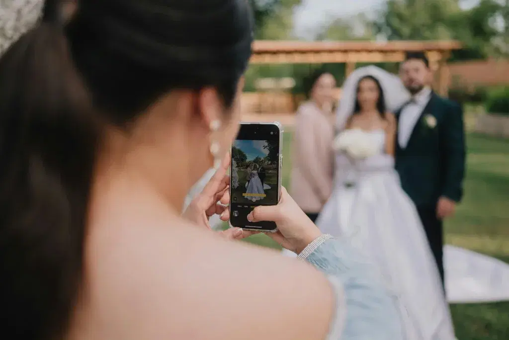 Woman photographing bride and groom with smartphone
